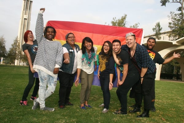 LGBTRC students laughing in front of Bell Tower with Pride flag.